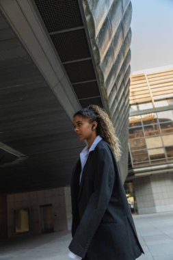 side view of african american woman in oversize suit listening music and walking on urban street in prague 