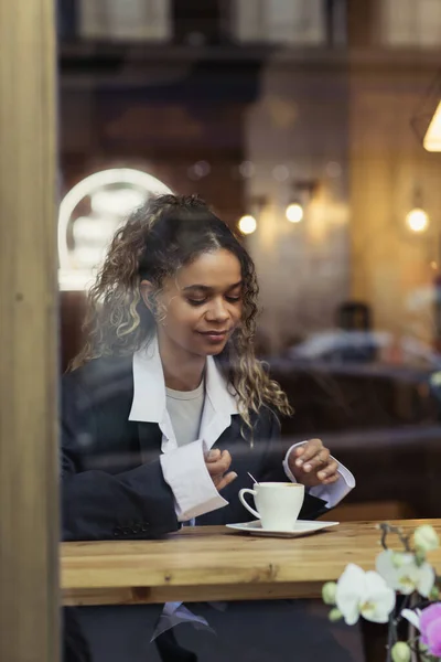 tattooed african american woman in wireless earphone listening music near cup of coffee in cafe