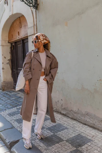 Full length of stylish african american woman in headscarf and sunglasses posing with reusable bag on street in prague — Fotografia de Stock