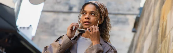 Stylish african american woman in trendy trench coat wearing sunglasses in street in prague, banner — Stockfoto