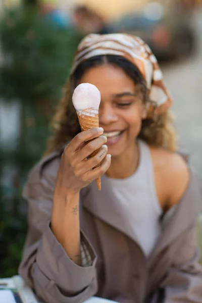 Tattooed african american woman in headscarf smiling while holding ice cream cone — Stockfoto