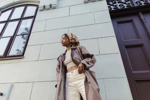 Full length of african american woman in trendy outfit and headscarf standing near building in prague - foto de stock