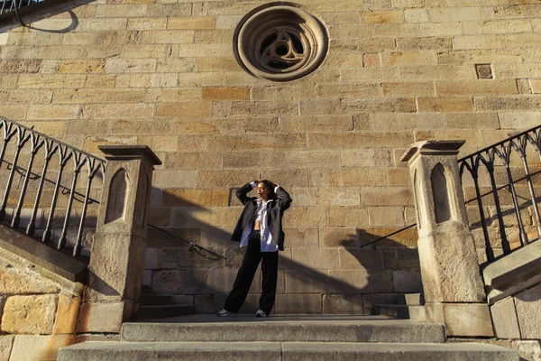 Full length of stylish african american woman in oversize suit standing near ancient wall in prague — Photo de stock