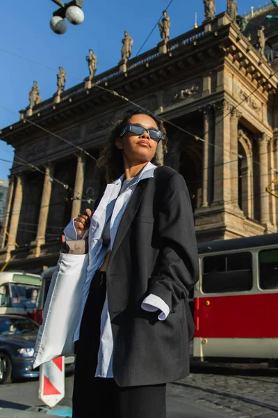 Low angle view of young african american woman in sunglasses posing near national theatre in prague — Stockfoto
