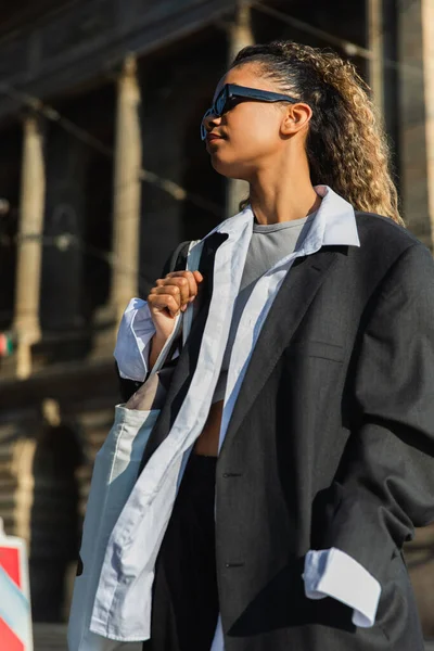 Low angle view of young african american woman in sunglasses posing near building in prague - foto de stock