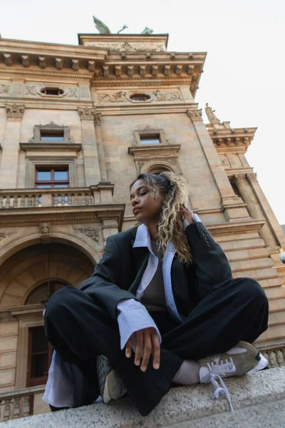 С низким углом зрения на африканскую американку в огромном костюме, сидящую со скрещенными ногами возле национального театра в Праге — стоковое фото