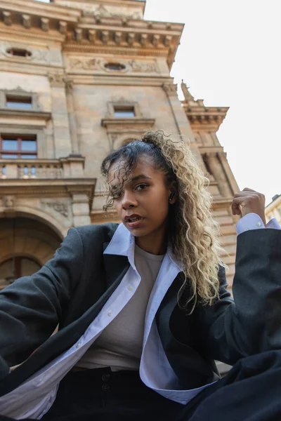 Low angle view of african american woman listening music in wireless earphone near national theatre in prague — Stock Photo