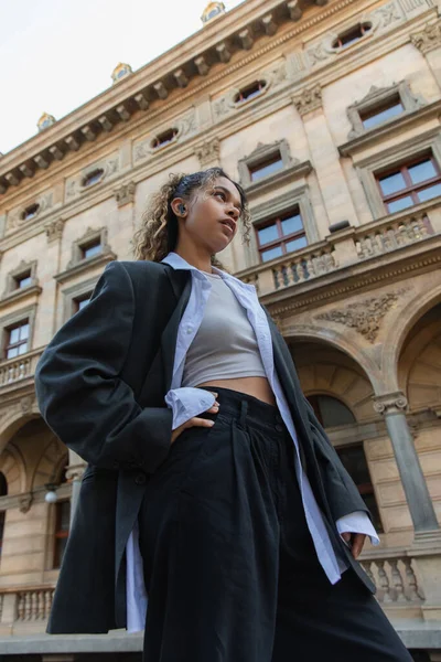 Low angle view of stylish african american woman in wireless earphone posing near national theater in prague — Stockfoto