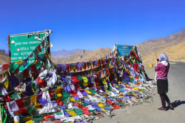 A women clicking photo of Tibetan Buddhist prayer flags at Fotu la Ladakh. Tibetan Buddhist Prayer Flag is inscribed with auspicious symbols, invocations, prayers, and mantras.