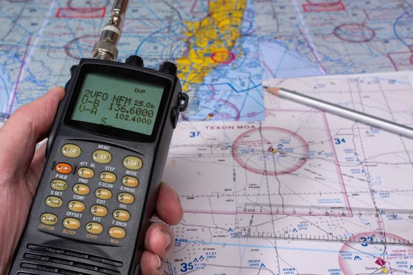 A man\'s hand holds a specialized receiver over a table with aviation maps.