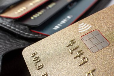 Banka kartlı bir plastik kartın makro çekimi, arka planda kartları olan deri bir cüzdan, seçici odaklanma. Para aktarımı kavramı.