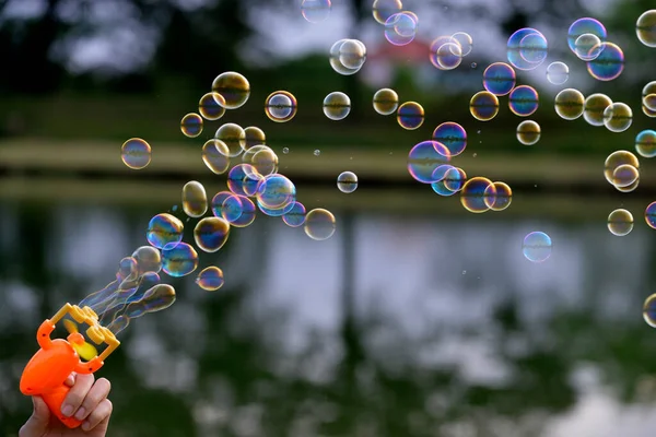 Rainbow color bubble are blowing from a bubble maker with dark blur lake background