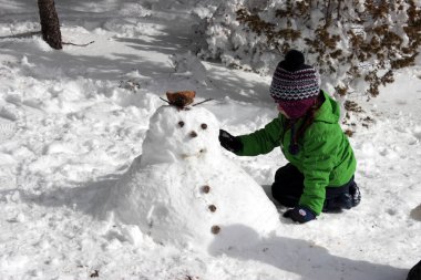 Girl making a snowman on a sunny winter day.