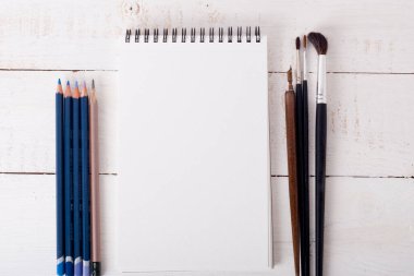 paper, calligraphy pen, brushes and pencils on white wooden tabl