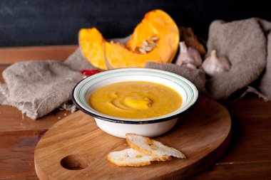 hot spice pumpkin soup with garlic, chili pepper, ginger on wooden table