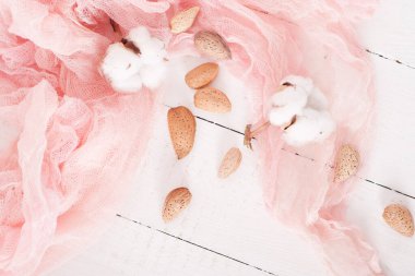 almonds and cotton with rose textile on whte wooden table