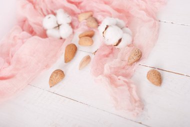 almonds and cotton with rose textile on whte wooden table