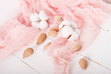 almonds and cotton with rose textile on whte wooden table
