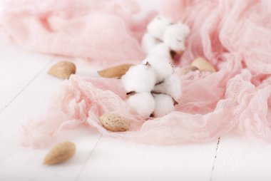 almonds and cotton with rose textile on whte wooden table