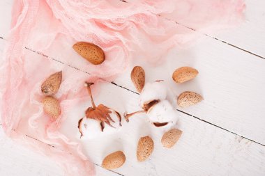 almonds and cotton with rose textile on whte wooden table