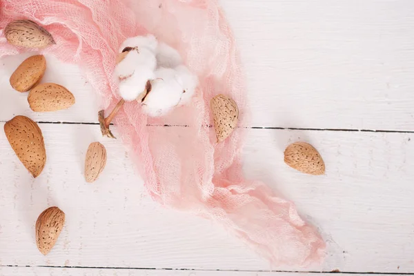 almonds and cotton with rose textile on whte wooden table