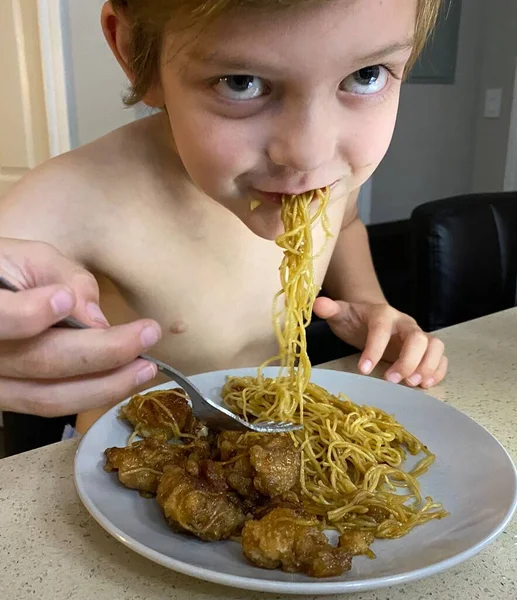 Boy enjoying some food. Young boy eating dinner or lunch. Boy eating noodles. Boy eating Chinese food.