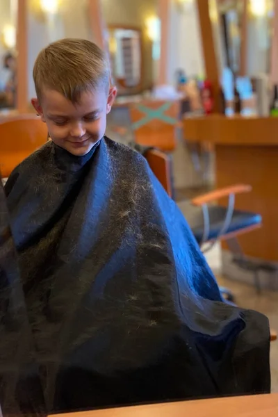 Boy getting his hair cut. Cute boy liking his haircut. Smiling boy at the barber shop.