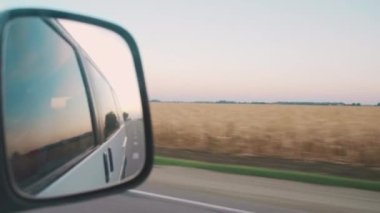 Sight from the passenger seat from the car window to the rearview mirror with yellow wheat fields. 4K