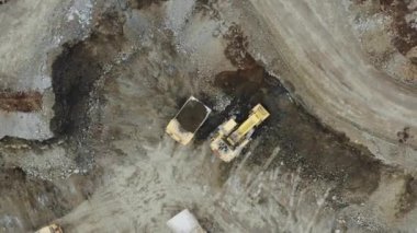 Yellow excavator in a quarry next to a heavy truck. View from the drone, vertical panorama in motion. 4K