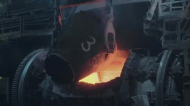 A stream of molten metal pours from the ladle into the furnace. Liquid metal production process. Molding molten metal in an industrial plant. 4K