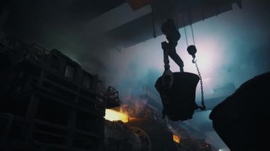 Hard work in the foundry. Pouring molten steel. The bucket on chains is moving through the plant. Steel manufacturing. Light hits through the smoke..4K