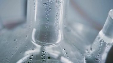 Close-up of misted glass flask with green liquid. Drops flow down the flask. Chemical reaction in the laboratory. Vertical panorama. Camera moves from bottom to top. 4K