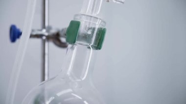 Drops slowly flow down the tube into the flask. Distillation process. Chemical reaction. Bright laboratory. Camera slowly moves from top to bottom. 4K