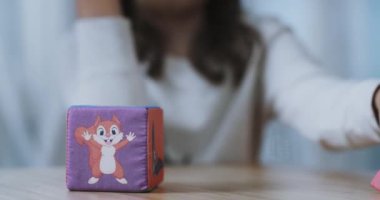 Two children's plush cubes with images of a squirrel, an elephant and a monkey. A girl puts one cube on another. Close-up. 
