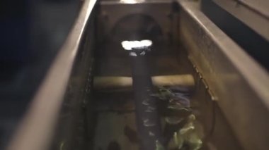 Cooling the cable in a special bath at the cable factory. Close-up. The camera moves quickly along the cable. Glare and reflections of light on the water. Production process. 4K