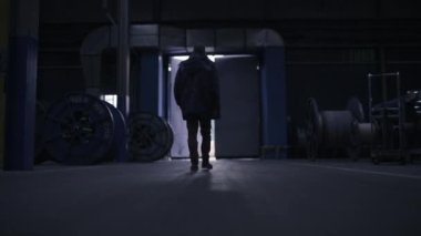 A male production worker goes through the factory to the exit. The camera behind follows him. Dark room, out into the light. A factory worker finishes his shift. 4K