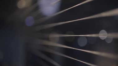 Close-up of stretched thin steel cables. Cable factory. The camera slowly moves along the cables to the steel reel. Dark background with round glare. Glare of light on the reel. 4K