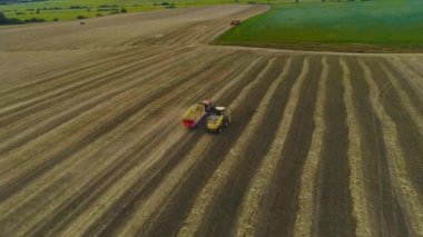 Bird's-eye view of a red tractor and a yellow combine harvester in the field. Harvesting wheat and rye. The camera flies closer to the harvester. Green meadows and fields in the background.4K