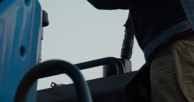 Mavi bir traktörün deposuna yakıt ikmali işlemi. Adam bir hortum tutuyor. Depoya benzin giriyor. 4K