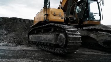 Sarı sürüngen kazıcı bir taş ocağından geçiyor. Kazıcının sürüngen tekerleklerine yakın çekim. Bir toprak dağı ve arka planda bulutlu bir gökyüzü. 4K