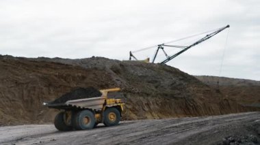 Taş ocağındaki toprak sürücüleriyle dolu nakliye kamyonu. Arka planda büyük bir zemin ve kazıcı vinç dağı var. Toprak kamyonun arkasından dökülüyor. Taş ocağı. 4K