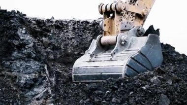 Kazı kovası kayaları topluyor. Yakın plan. Yüksek kontrastlı görüntü. Temiz beyaz gökyüzü. Taş ocağında çalışma süreci. 4K