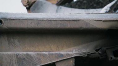 Kazı makinesinin metal kovası cesede taş atıyormuş. Kamera kovayı takip ediyor. Arka planda gri gökyüzü. 4K