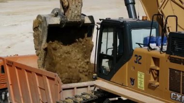 Sarı bir kazıcı toplanan toprağı kırmızı bir kamyonun arkasına boşaltıyor. Yakın plan. Arka planda sürücüler yüklü başka bir kamyon daha var. Taş ocağı. 4K