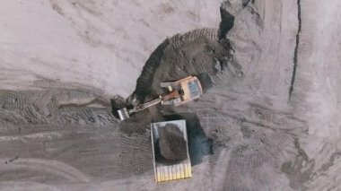 Zemini kazan ve kamyonun arkasına boşaltan sarı bir sürüngen kazıcısının üst görüntüsü. Kamera dönüyor ve alçalıyor. Taş ocağında çalışma süreci. 4K
