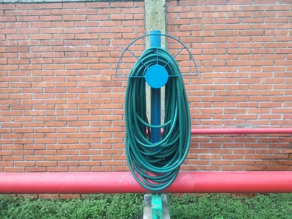 Yeşil su hortumu kırmızı tuğla duvara dolandı. Boşluğu kopyala