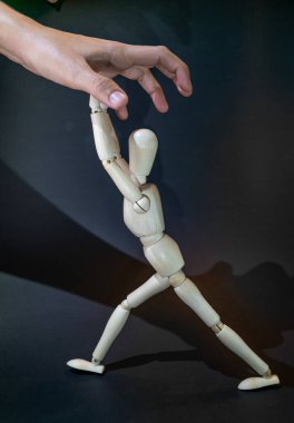 a wooden dummy fights against a human hand tryingto grasp it. black background