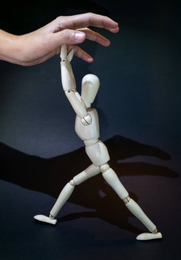 a wooden dummy fights against a human hand tryingto grasp it. black background