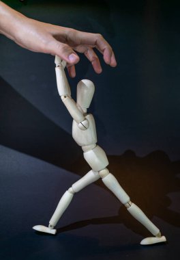 a wooden dummy fights against a human hand tryingto grasp it. black background