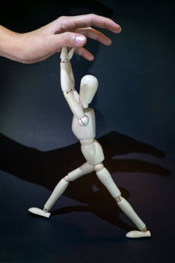 a wooden dummy fights against a human hand tryingto grasp it. black background